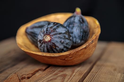 Fresh purple figs in a bowl on a wooden background from old boards. Raw exotic figs. Low key