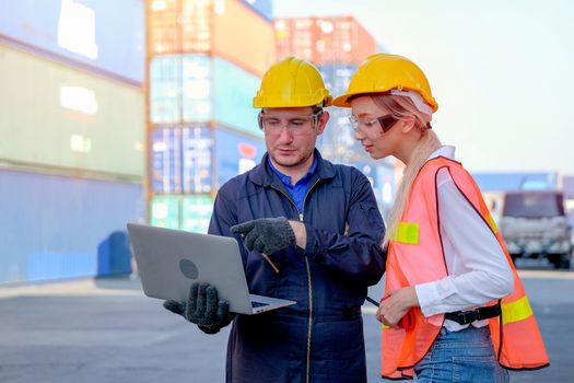Technician worker man point to laptop and discuss with his worker woman in cargo container shipping area.