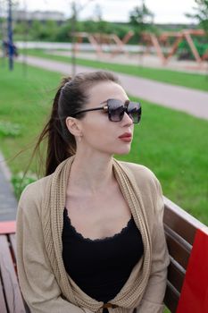 attractive brunette woman sitting on a bench in park. fashion clothes, stylish look.