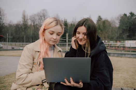 Two woman seat in the park with laptop and watch. LGBT