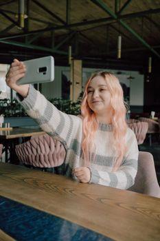 Young woman sitting in a cozy coffehouse drinking coffee and using her smartphone.