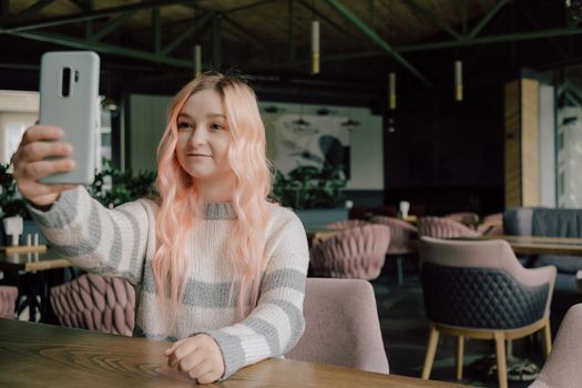 Young woman sitting in a cozy coffehouse drinking coffee and using her smartphone.