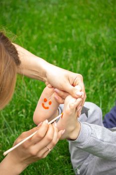 child sitting on the grass, smiling on the child's leg with paints