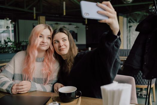 Cheerful young lesbian couple selfie using mobile phone at a coffee shop. Two joyful attractive Asian girls together at restaurant or cafe. Holiday activity, or modern lifestyle concept.