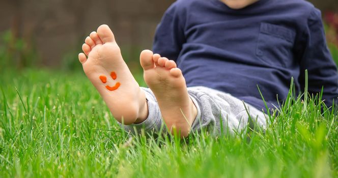 child sitting on the grass, smiling on the child's leg with paints