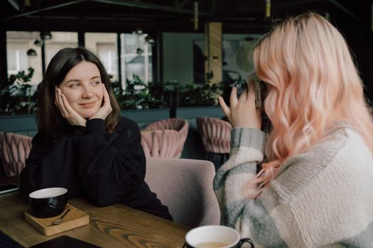 Lesbian couple taking photo of each other on a camera in cafe. art