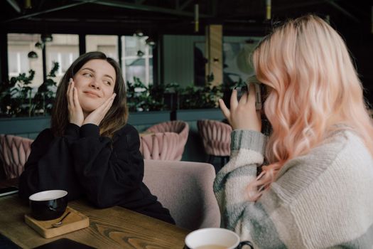 Lesbian couple taking photo of each other on a camera in cafe. art