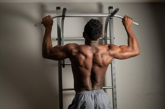 African american man with naked torso pulls up on horizontal bar in gym