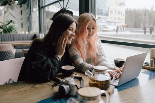 two happy young women sitting in coffee shop looking at laptop computer together.