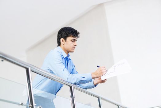 Portrait of a young businessman, something he writes in the document, rests on a metal railing