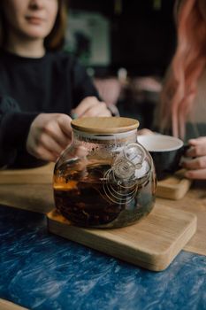 Young woman in cafe during quarantine. Girl pouring some tea from teapot into white cup. Beautiful woman in green sweater smile. Alone in kitchen.