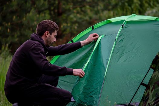 a man sits near a tourist tent. Nature, recreation, camping. Selective focus