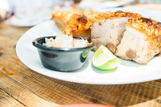 45 degree view of a plate of chicharron served with onion and lime on a plate on a wooden table with some copy space.