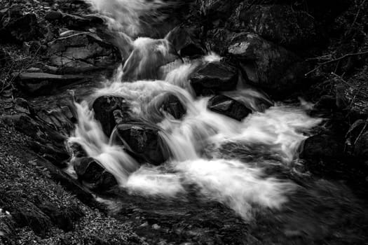 Black and white view of water stream between rocks. Close up