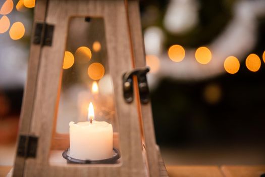 The peaceful flame of a burning candle against a background of fuzzy Christmas tree lights. Christmas atmosphere of the holidays in December.