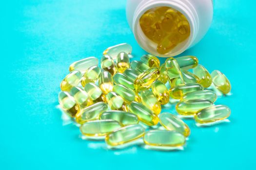 Omega 3 fish oil capsules spilling out of a bottle on a blue background.