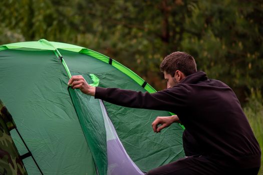 a man sits near a tourist tent. Nature, recreation, camping. Selective focus