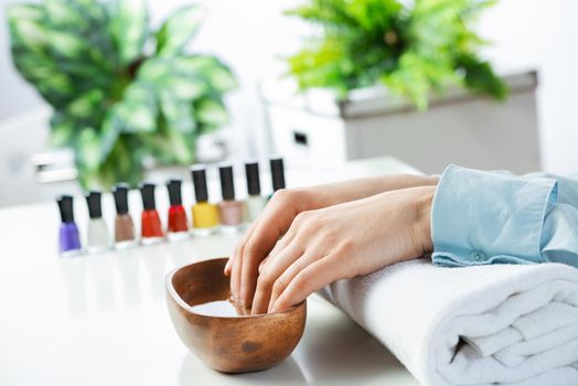 Closeup female hands in wooden bowl with water. Spa procedure and relaxation. Female hands preparing for manicure. Professional nail care and beautician service. Beauty and hygiene concept