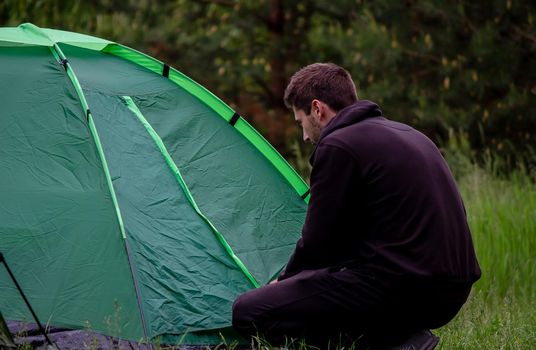 a man sits near a tourist tent. Nature, recreation, camping. Selective focus