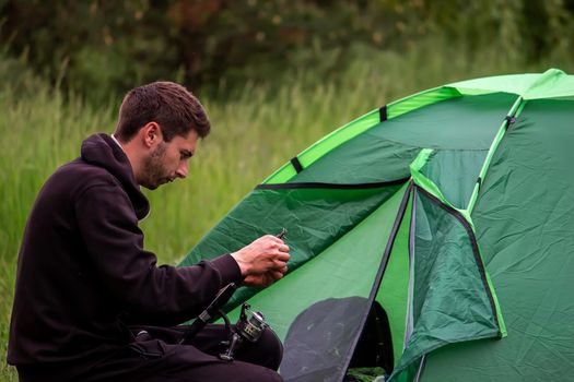 a man sits near a tourist tent. Nature, recreation, camping. Selective focus