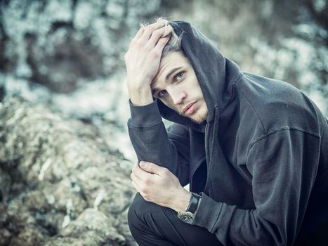 Portrait of young man in hoodie posing outdoor in winter setting with snow all around, looking at camera.