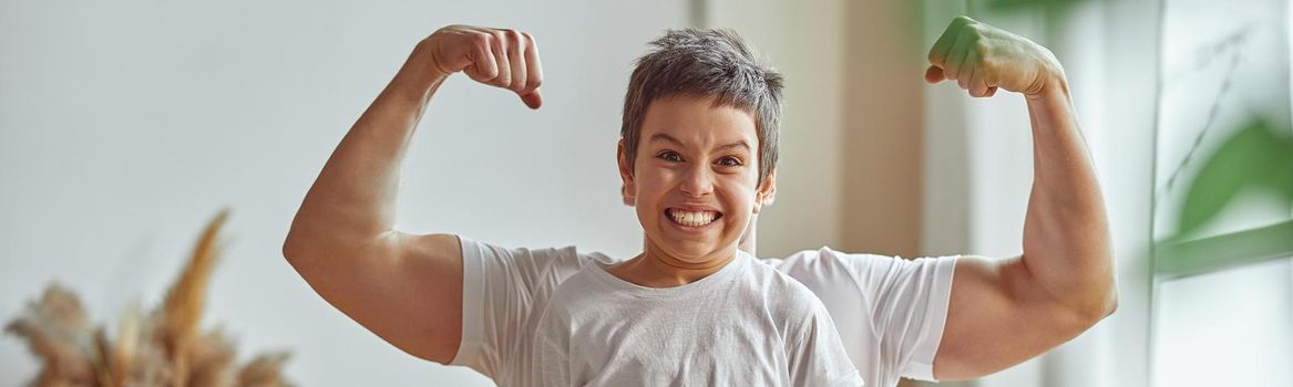 Waist up portrait of smiling son standing before dad who is demonstrating his biceps muscles