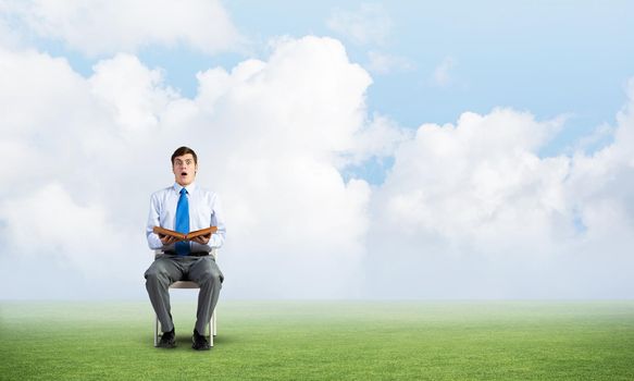 young businessman with book on office chair