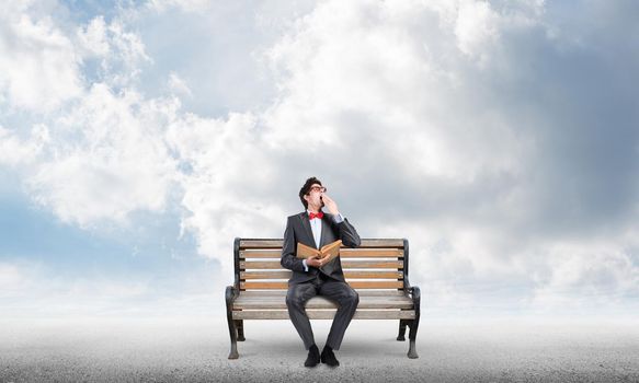 Student sits on a bench, holding a book. Traditional education concept