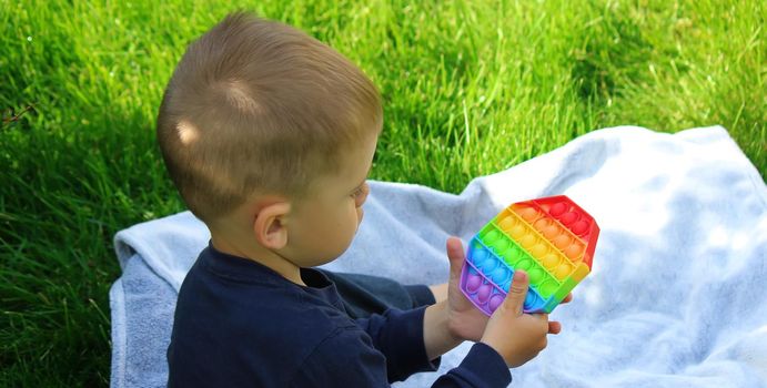 Pop it silicone anti-stress toy. The child plays on the grass. New trend Selective focus. Nature