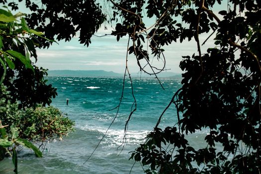 Cinematic scenery of the tropical blue sea and sky framed by tree branches during the summer in Koh rong Island, Cambodia