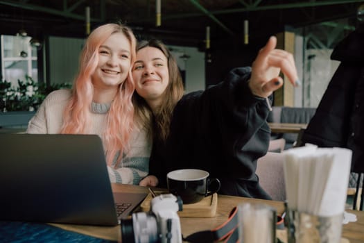 two happy young women sitting in coffee shop looking at laptop computer together.
