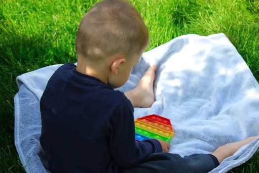 Pop it silicone anti-stress toy. The child plays on the grass. New trend Selective focus. Nature