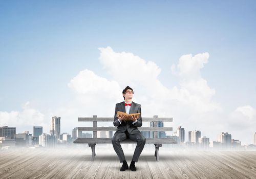 Student sits on a bench, holding a book. Traditional education concept