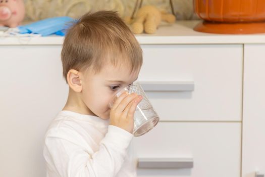 The child drinks water from a glass. Selective focus.