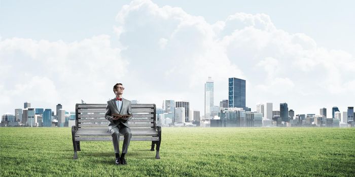 Funny man in red glasses and suit sitting on bench and reading book