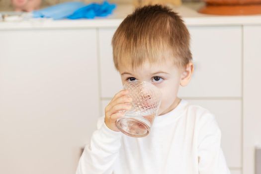 The child drinks water from a glass. Selective focus.