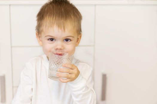 The child drinks water from a glass. Selective focus.