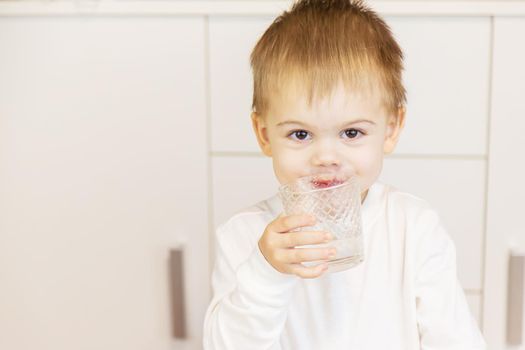The child drinks water from a glass. Selective focus.
