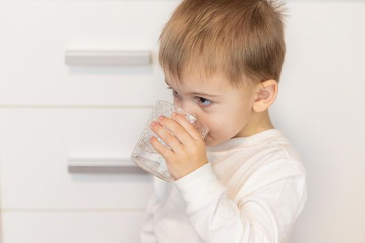 The child drinks water from a glass. Selective focus.