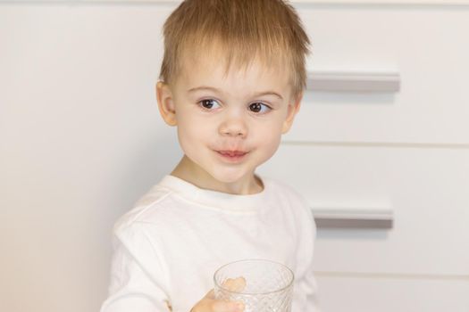The child drinks water from a glass. Selective focus.