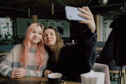 Cheerful young lesbian couple selfie using mobile phone at a coffee shop. Two joyful attractive Asian girls together at restaurant or cafe. Holiday activity, or modern lifestyle concept.