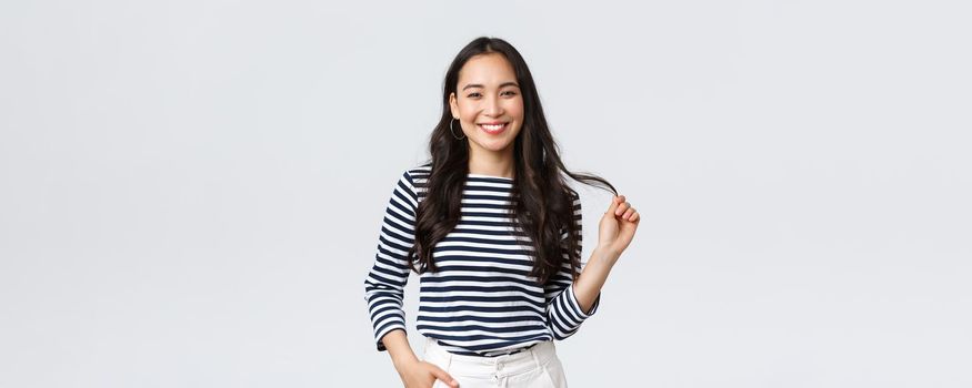 Lifestyle, people emotions and casual concept. Stylish beautiful smiling asian woman touching hair strand, made new haircut or bought good haircare product, standing white background.