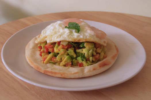 Simple and healthy vegetarian breakfast of pita bread with fresh avocado and tomato salad topped with fried egg