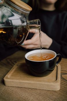 Young woman in cafe during quarantine. Girl pouring some tea from teapot into white cup. Beautiful woman in green sweater smile. Alone in kitchen.