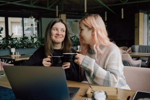 two happy young women sitting in coffee shop looking at laptop computer together.