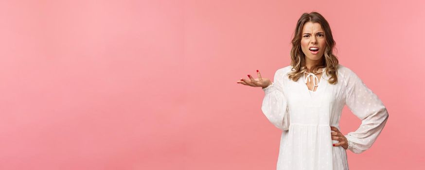 Whats your problem. Pissed-off and annoyed young blond girl looking questioned, cant understand what person complain about, raise on hand in dismay, shrug and grimace puzzled, pink background.