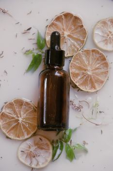 Product photo of a glass dropper bottle containing natural anti aging serum sat against an aromatic milk bath containing dried citrus and herbs