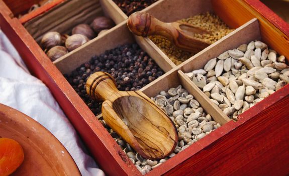 Various exotic spices and condiments in boxed compartments used in eastern cooking with wooden serving spoons