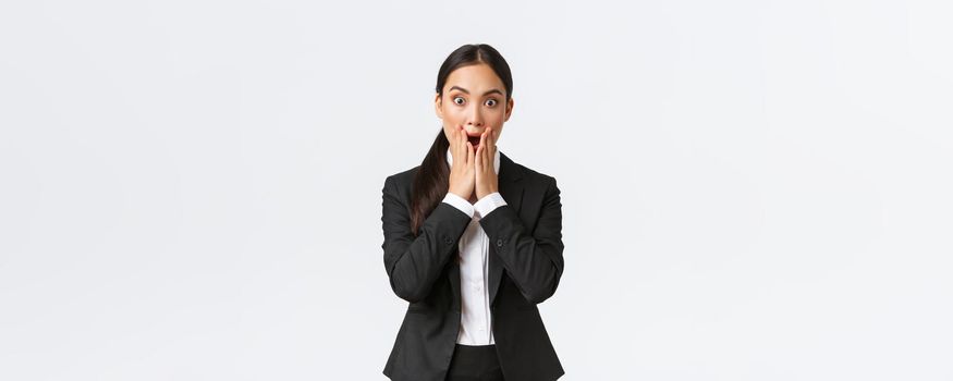Shocked concerned asian businesswoman facing troublesome situation, drop jaw and stare startled at camera, dont know what do, feeling panic and shook, standing white background.