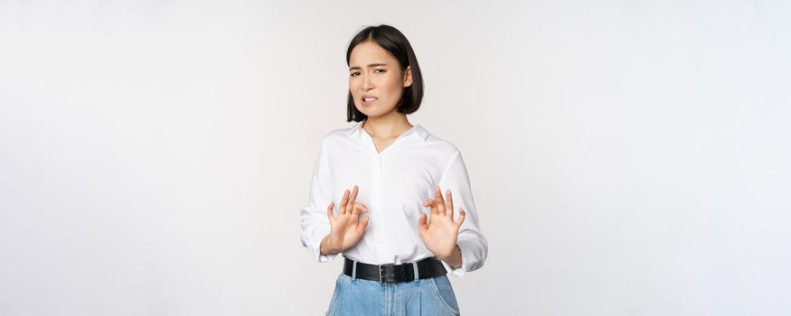 No thank you. Young disgusted asian woman declining proposal, shaking hands and step back, looking with dislike, rejecting offer, standing over white background.